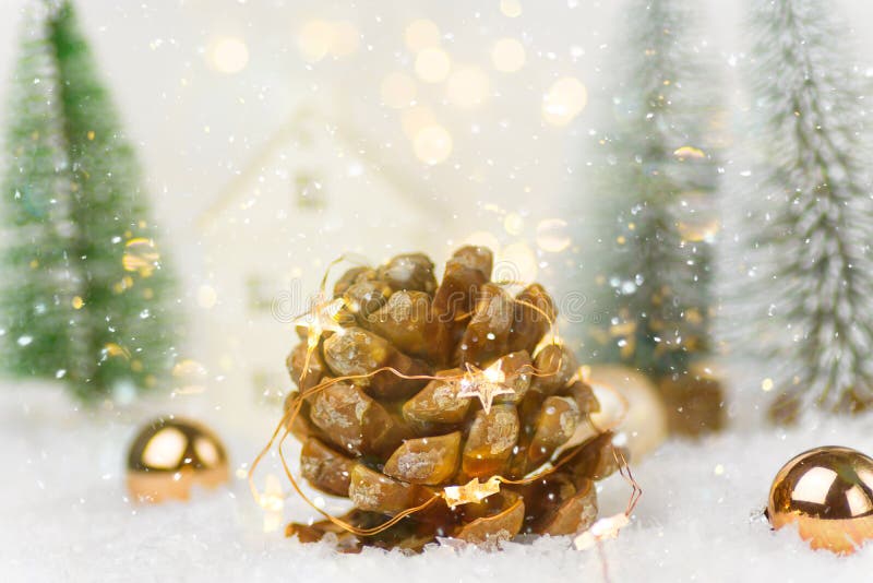 Big pine cone with golden garland lights in winter scene in forest with fir trees falling snow. Christmas New Years holiday magic
