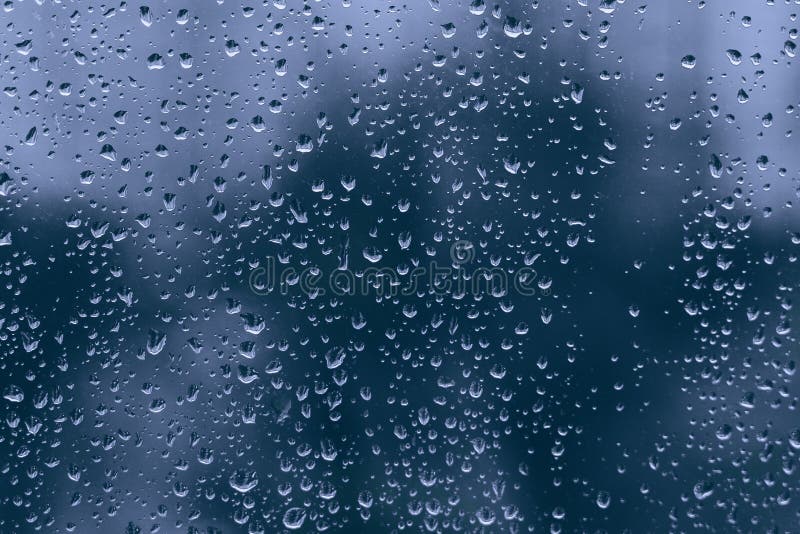 Big rainy droplets on a blue black glass window surface. water drops on dripped background pane in a rainy days in night city wet