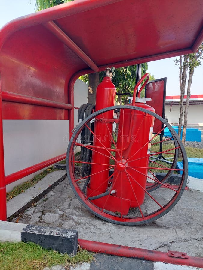 A big red fire extinguisher with two wheels on the side that often sits on the edge of a gas station stock photo
