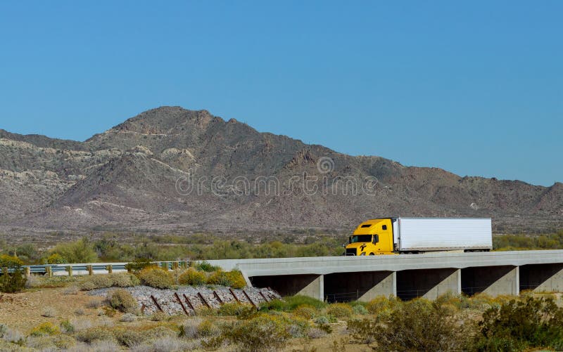 Big rig long haul semi truck with two flat bed semi trailers transporting on the winding road with bridge around the mountain rock