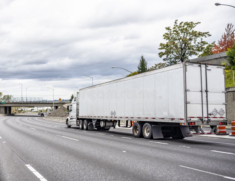 Big rig white long haul semi truck with dry van semi trailer running on the turning highway road with bridge ahead