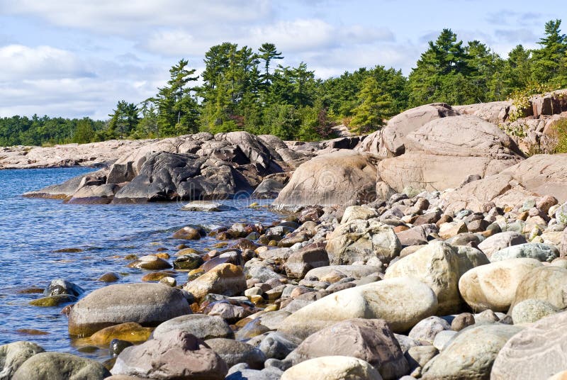 A lake shore filled with big rocks and evergreen trees.