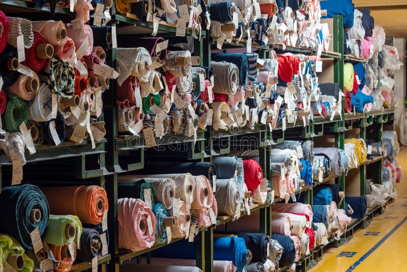 Big rolls of colorful fabric stacked on factory shelves ready for production