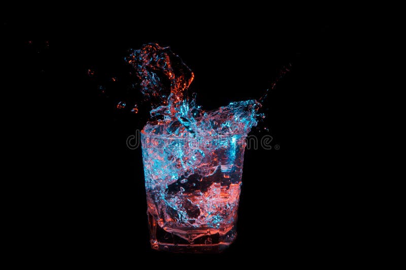 Big splash in a rocks glass under blue and orange lights isolated on a black background