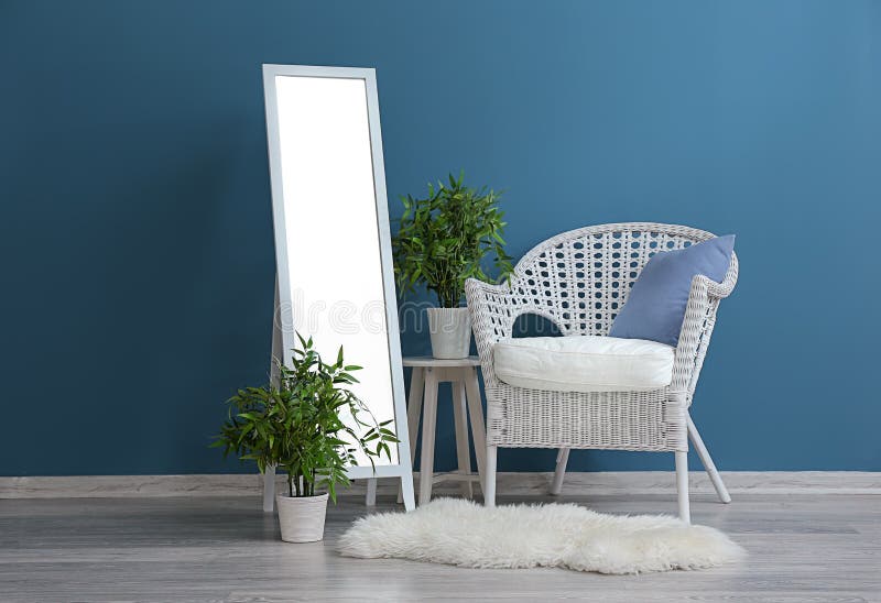 Big stylish mirror with armchair and plants near color wall in room