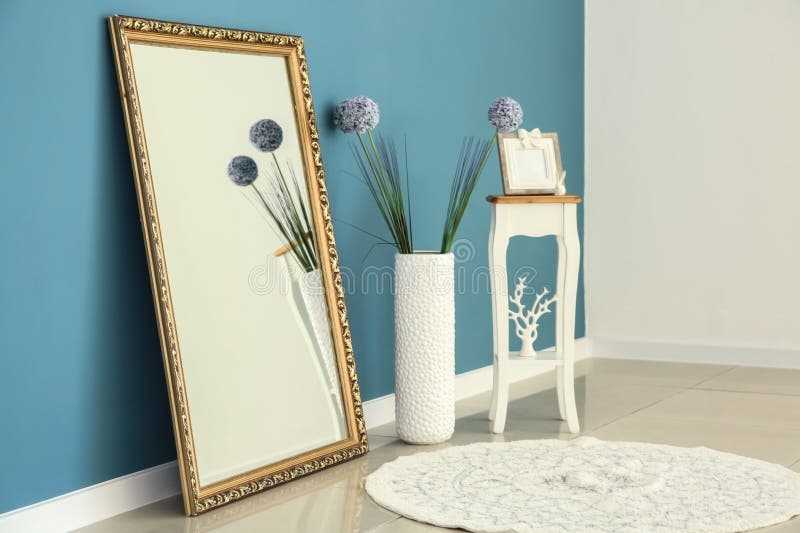 Big stylish mirror with small table and vase near color wall in room