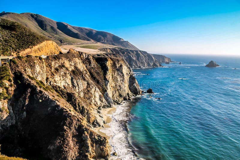 Big Sur is a sparsely populated region of the Central Coast of California where the Santa Lucia Mountains rise abruptly from the Pacific Ocean. The name Big Sur is derived from the original Spanish-language el sur grande, meaning the big south, or from el paÃ­s grande del sur, the big country of the south, referring to its location south of the Monterey Peninsula. The terrain offers stunning views, making Big Sur a popular tourist destination. Big Sur's Cone Peak is the highest coastal mountain in the contiguous 48 states, ascending nearly a mile (5,155 feet/1571 m) above sea level, only three miles (4.8 km) from the ocean. Wikipedia. Big Sur is a sparsely populated region of the Central Coast of California where the Santa Lucia Mountains rise abruptly from the Pacific Ocean. The name Big Sur is derived from the original Spanish-language el sur grande, meaning the big south, or from el paÃ­s grande del sur, the big country of the south, referring to its location south of the Monterey Peninsula. The terrain offers stunning views, making Big Sur a popular tourist destination. Big Sur's Cone Peak is the highest coastal mountain in the contiguous 48 states, ascending nearly a mile (5,155 feet/1571 m) above sea level, only three miles (4.8 km) from the ocean. Wikipedia