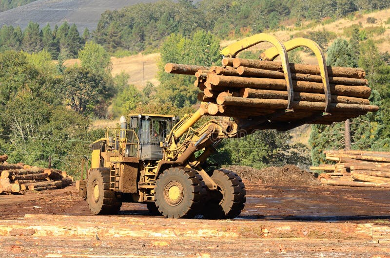 A large wheeled loader unloads a log truck at a small log sawmill in Oregon. Claw machine stock images, royalty-free photos and pictures