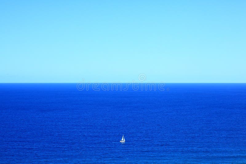 Big blue ocean with small white sailing boat, vastness