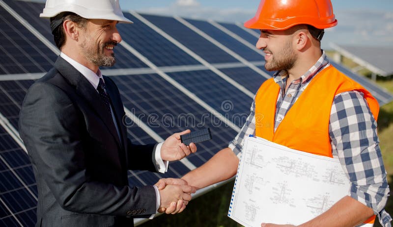 At solar energy station business client and foreman shaking hands. Two men making deal, shaking hands, solar panels on backstage. At solar energy station business client and foreman shaking hands. Two men making deal, shaking hands, solar panels on backstage.