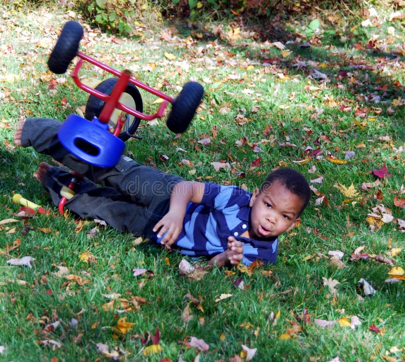 A young boy falls off his bike while riding on the grass. A young boy falls off his bike while riding on the grass.