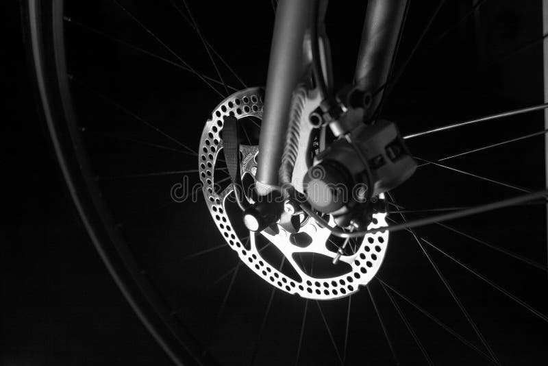 Front tire on a bike on black background, showing tire, rim, spokes and shinny disc brakes - an alternative form of human powered transportation - environmentally friendly. Front tire on a bike on black background, showing tire, rim, spokes and shinny disc brakes - an alternative form of human powered transportation - environmentally friendly