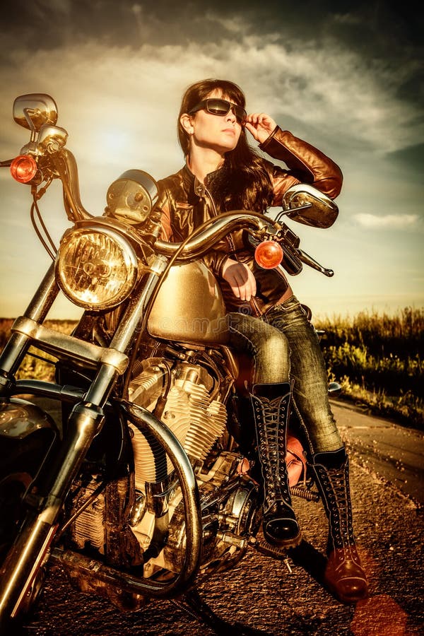 Biker girl in una giacca di pelle su una moto guardando il tramonto.