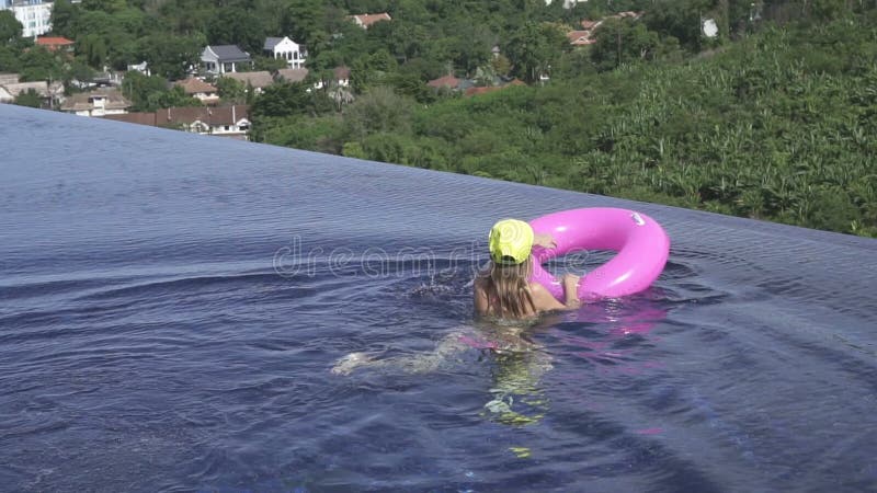 Bikini d'uso della giovane donna graziosa, cappello giallo ed occhiali da sole porpora nuotanti con l'anello gonfiabile rosa nell