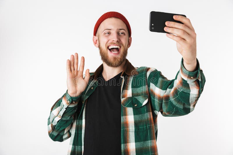 Bild av den bärande hatten för caucasian grabb och plädskjortan som tar selfiefotoet på mobiltelefonen, medan stå isolerat över v royaltyfri fotografi Bild av den bärande hatten för caucasian grabb och plädskjortan som tar selfiefotoet på mobiltelefonen, medan stå isolerat över v royaltyfri fotografi