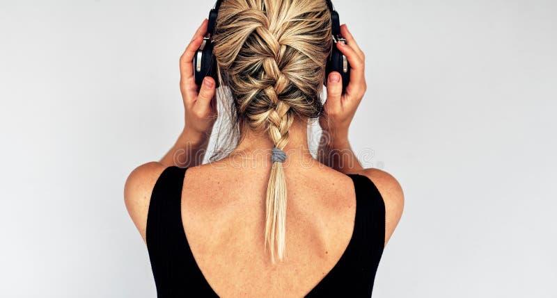 Bild av en blond ung kvinna som rör hennes hörlurar när hon lyssnar på musik. horisontell bakvy av ganska kvinnlig fotografering för bildbyråer