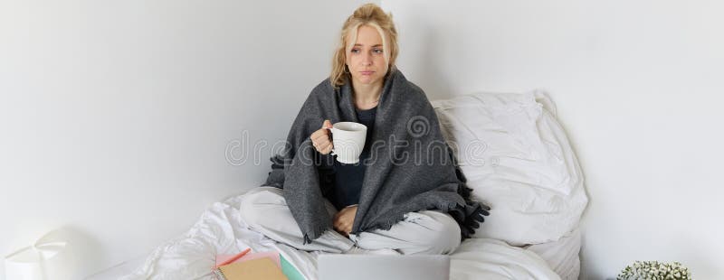 Portrait of woman catching a flu, sneezing, feeling sick, sitting on bed with laptop and working on remote while caught a cold. Portrait of woman catching a flu, sneezing, feeling sick, sitting on bed with laptop and working on remote while caught a cold.