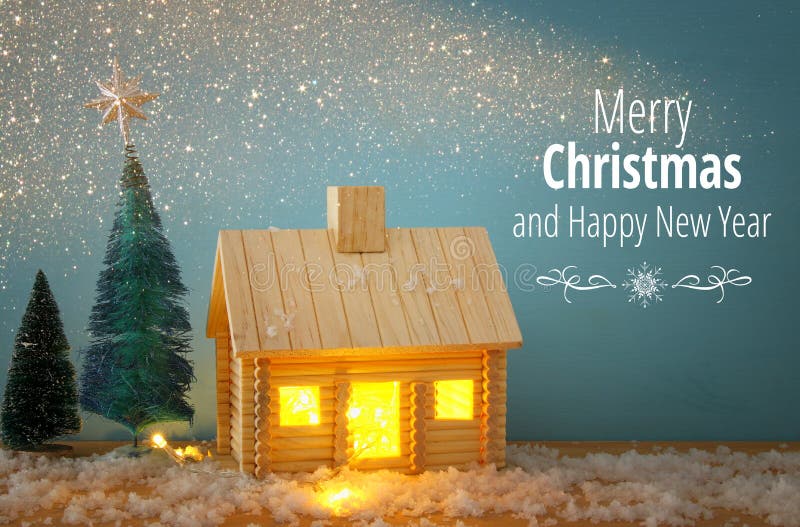 Bild av julträdet och trähuset med ljus till och med fönstret, över den snöig tabellen arkivbild Bild av julträdet och trähuset med ljus till och med fönstret, över den snöig tabellen arkivbild