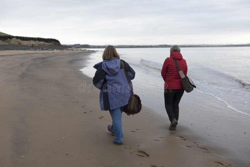 Bild der hinteren Ansicht eines reifen weiblichen Paares, das entlang den Strand geht stockbilder Bild der hinteren Ansicht eines reifen weiblichen Paares, das entlang den Strand geht stockbilder