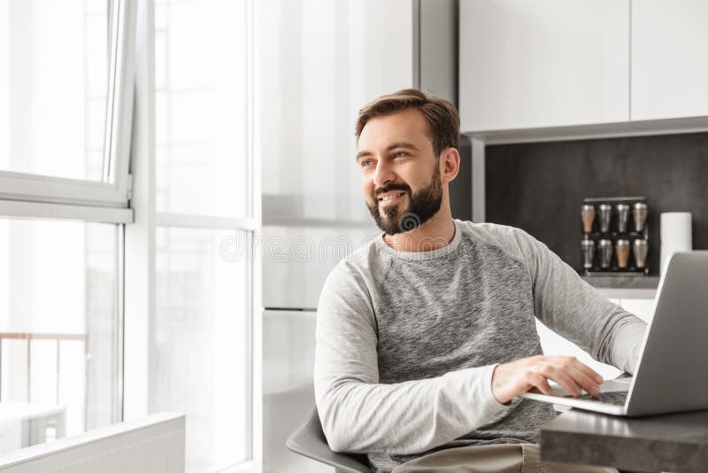 Bild des freudigen Mannes 30s im zufälligen Hemd, das an Laptop an h arbeitet stockfoto Bild des freudigen Mannes 30s im zufälligen Hemd, das an Laptop an h arbeitet stockfoto