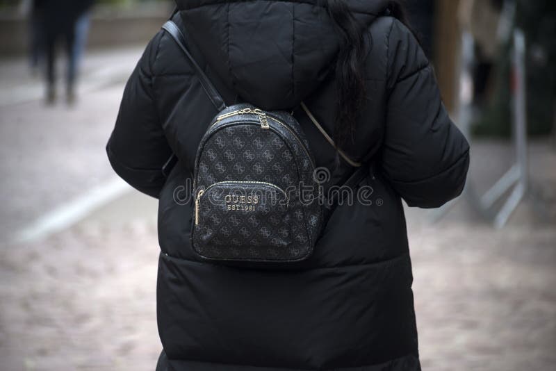 Colmar - France - 9 december 2022 - Portrait on back view of woman with a Guess backpack standing in the street. Colmar - France - 9 december 2022 - Portrait on back view of woman with a Guess backpack standing in the street