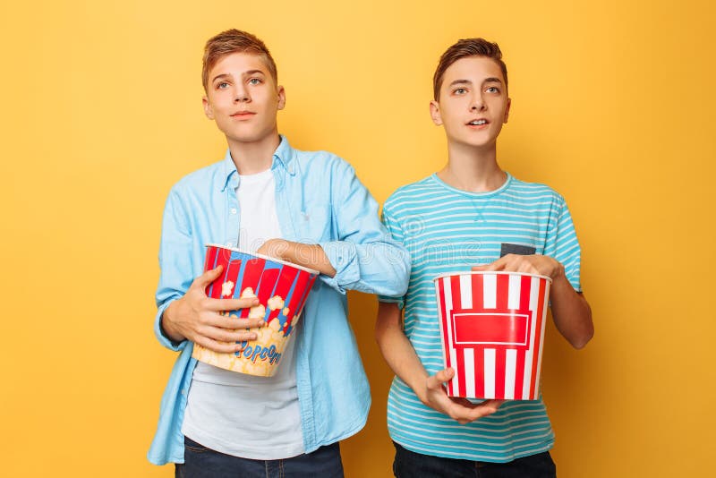 Bild von zwei regte schöne Jugendliche, die Kerle auf, die einen interessanten Film aufpassen und Popcorn auf einem gelben Hinter lizenzfreies stockbild Bild von zwei regte schöne Jugendliche, die Kerle auf, die einen interessanten Film aufpassen und Popcorn auf einem gelben Hinter lizenzfreies stockbild