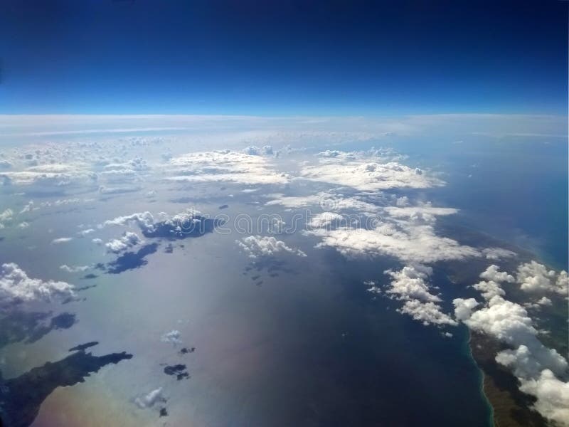Bilden av jorden med blå himmel och vit fördunklar över havet med solen reflekterad på vattnet och de lilla öarna arkivfoton Bilden av jorden med blå himmel och vit fördunklar över havet med solen reflekterad på vattnet och de lilla öarna arkivfoton