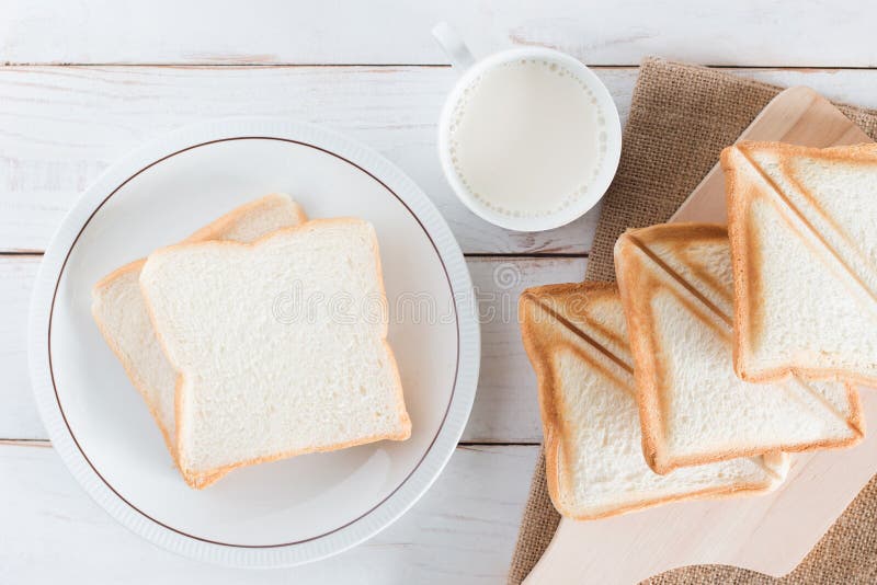 Bilden för den bästa sikten av Baked bröd och skivat bröd på skärbräda och maträtten med varmt mjölkar i den vita koppen på vit t royaltyfria bilder Bilden för den bästa sikten av Baked bröd och skivat bröd på skärbräda och maträtten med varmt mjölkar i den vita koppen på vit t royaltyfria bilder