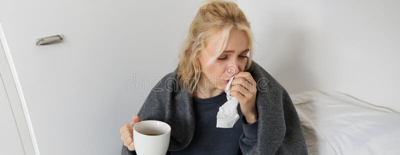 Portrait of woman catching a cold, staying home sick, drinking tea, sneezing in napkin, blowing nose, has covid symptoms. Portrait of woman catching a cold, staying home sick, drinking tea, sneezing in napkin, blowing nose, has covid symptoms.