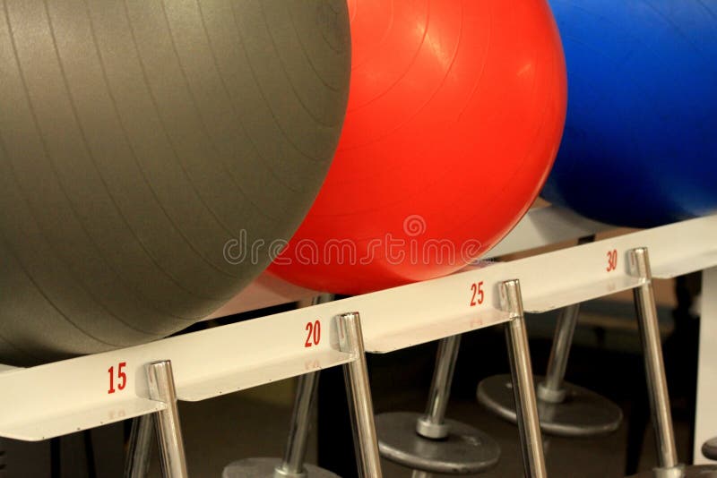 Exercise balls and gym weights on a rack at a fitness center, different sizes of weights and different colors of exercise balls are visible in the gym. Exercise balls and gym weights on a rack at a fitness center, different sizes of weights and different colors of exercise balls are visible in the gym.