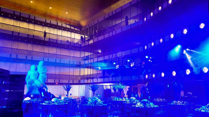 Binnen een feestelijke banketzaal, met blauwe en oranje verlichting, een marmeren standbeeld, vleklichten, en een paar mensen op stock afbeeldingen Binnen een feestelijke banketzaal, met blauwe en oranje verlichting, een marmeren standbeeld, vleklichten, en een paar mensen op stock afbeeldingen