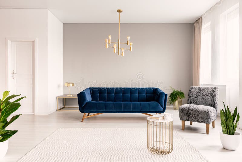 Binnenland van de exemplaar het ruimtewoonkamer met een donkerblauwe laag, een grijze leunstoel en gouden accenten Echte foto stock foto's Binnenland van de exemplaar het ruimtewoonkamer met een donkerblauwe laag, een grijze leunstoel en gouden accenten Echte foto stock foto's