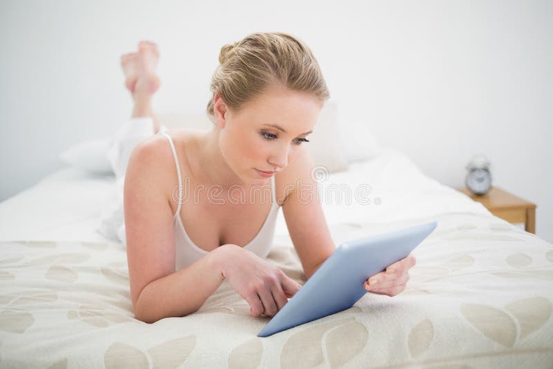 Bionda contenta naturale che si trova sul letto facendo uso della compressa immagine stock libera da diritti Bionda contenta naturale che si trova sul letto facendo uso della compressa immagine stock libera da diritti