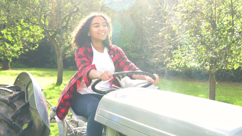 Biracial молодая женщина девочка-подростка управляя серым трактором через солнечный яблоневый сад