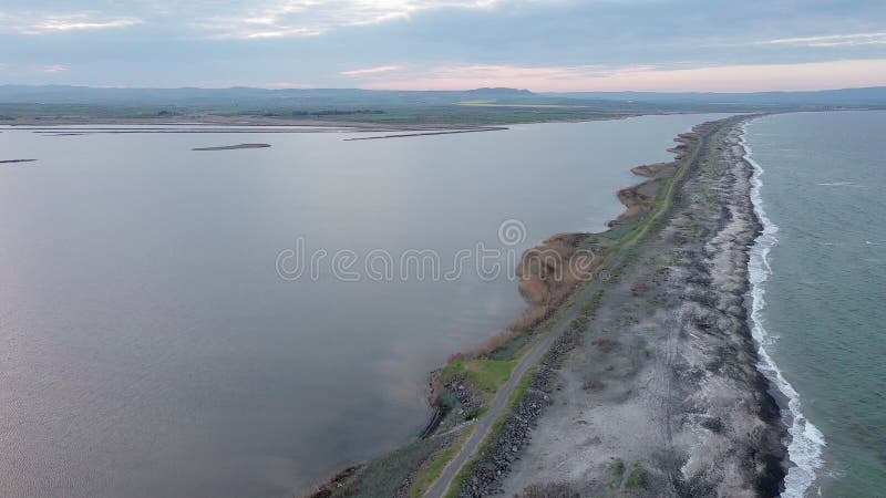 Bird&#x27;s eye view of beach with sand, grass and stones washed by bay of Black Sea and lake under sky in sunset light