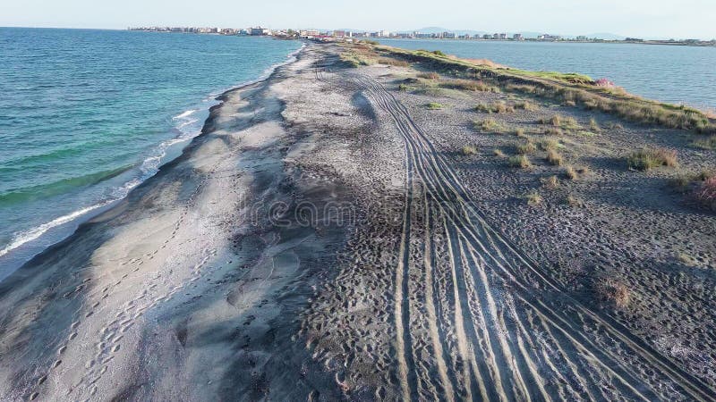 Bird&#x27;s eye view of beach with sand, grass and stones washed by bay of Black Sea and lake under sky in sunset light