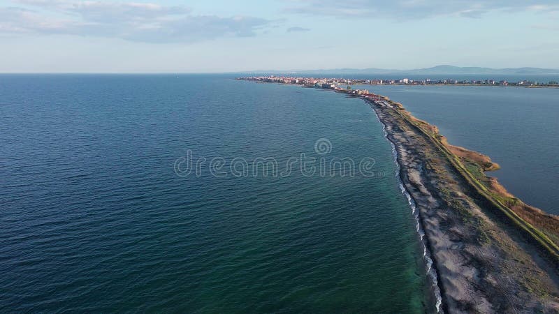 Bird&#x27;s eye view of beach with sand, grass and stones washed by bay of Black Sea and lake under sky in sunset light