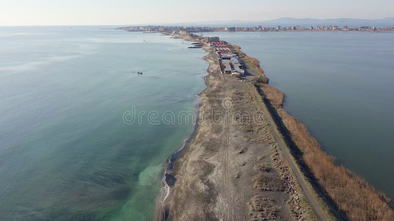 Bird&#x27;s eye view of beach with sand, grass and stones washed by bay of Black Sea and lake under sky in sunset light