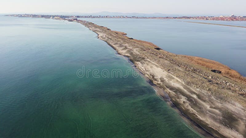 Bird&#x27;s eye view of beach with sand, grass and stones washed by bay of Black Sea and lake under sky in sunset light