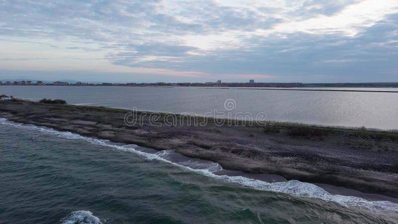 Bird&#x27;s eye view of beach with sand, grass and stones washed by bay of Black Sea and lake under sky in sunset light