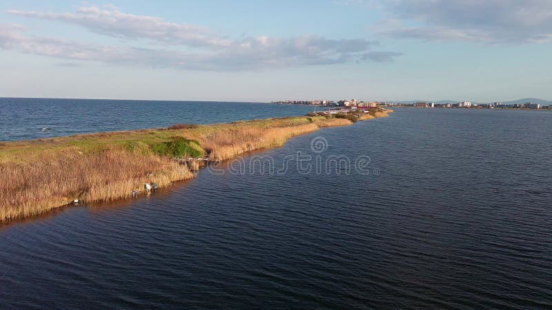 Bird&#x27;s eye view of beach with sand, grass and stones washed by bay of Black Sea and lake under sky in sunset light