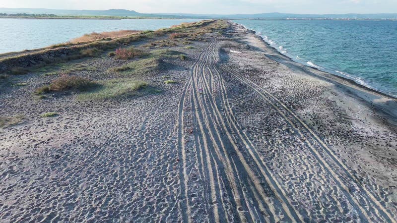 Bird&#x27;s eye view of beach with sand, grass and stones washed by bay of Black Sea and lake under sky in sunset light