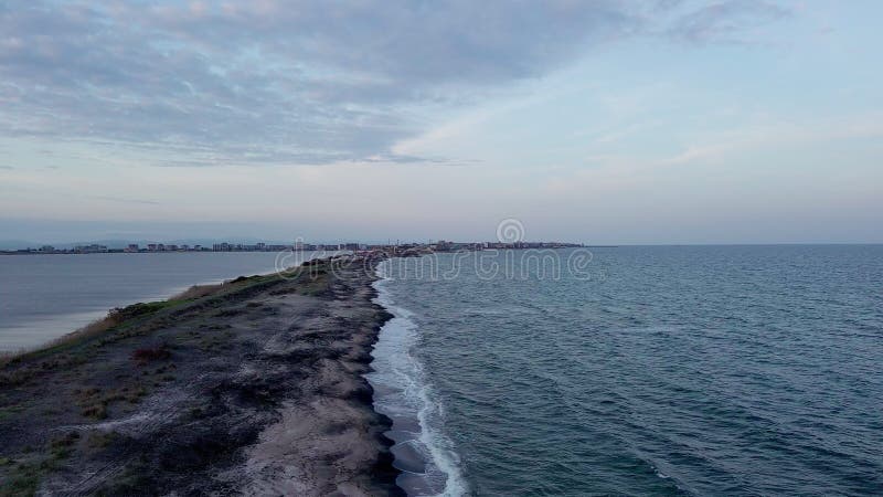 Bird&#x27;s eye view of beach with sand, grass and stones washed by bay of Black Sea and lake under sky in sunset light