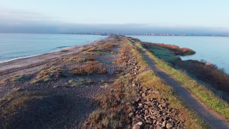 Bird&#x27;s eye view of beach with sand, grass and stones washed by bay of Black Sea and lake under sky in sunset light