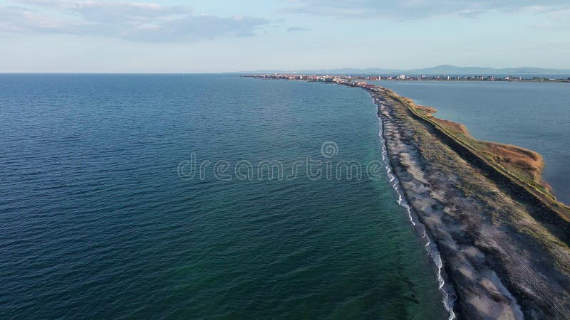 Bird&#x27;s eye view of beach with sand, grass and stones washed by bay of Black Sea and lake under sky in sunset light