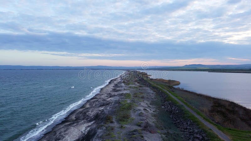 Bird&#x27;s eye view of beach with sand, grass and stones washed by bay of Black Sea and lake under sky in sunset light