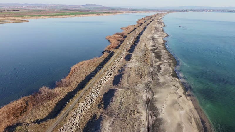 Bird&#x27;s eye view of beach with sand, grass and stones washed by bay of Black Sea and lake under sky in sunset light