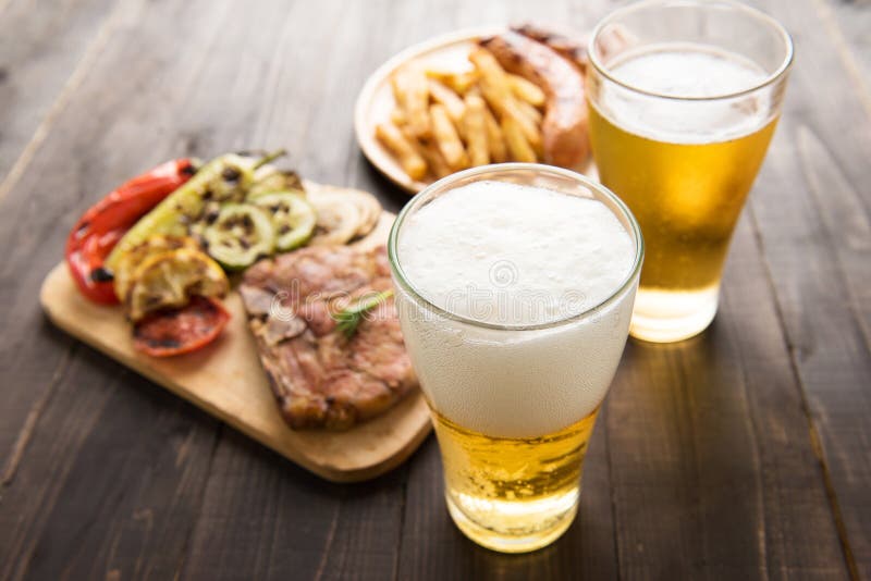 Birra in vetro con bistecca e le patate fritte gastronomiche sulla parte posteriore di legno fotografia stock libera da diritti Birra in vetro con bistecca e le patate fritte gastronomiche sulla parte posteriore di legno fotografia stock libera da diritti