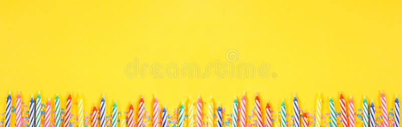 Birthday cake candles with candy sprinkles. Top down view banner with bottom border on a yellow background. Copy space. Birthday cake candles with candy sprinkles. Top down view banner with bottom border on a yellow background. Copy space