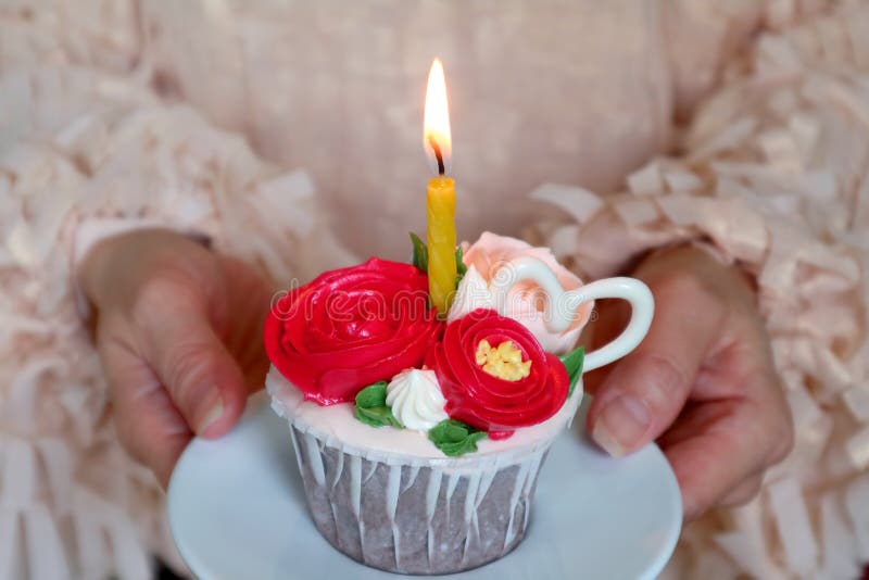 Birthday cake decorated with gorgeous flowers shaped whipped cream with a shining candle in woman` s hand.